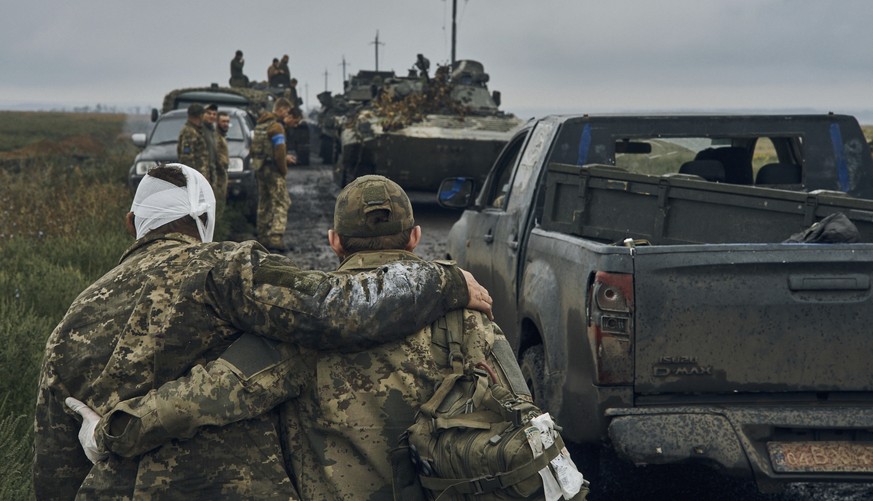 A Ukrainian soldier helps his wounded fellow soldier while military vehicles move on the road in the freed territory in the Kharkiv region, Ukraine, Monday, Sept. 12, 2022. Ukrainian troops retook a w ...