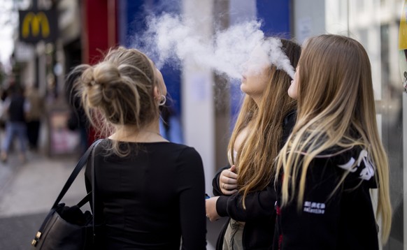 epa10663276 Young people use single-use vaping products in London, Britain, 30 May 2023. The UK government has announced it is cracking down on retailers providing free vape samples to children. The g ...