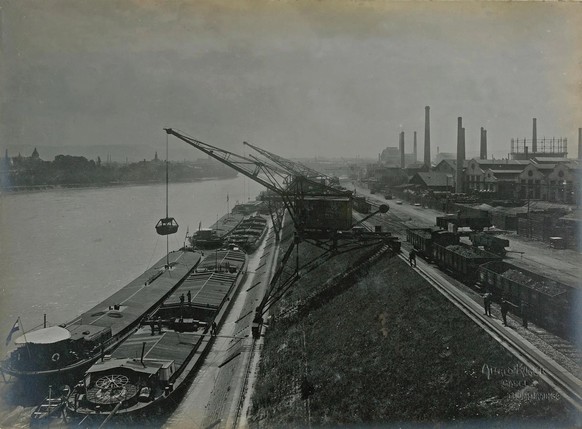 Kräne laden im Hafen St. Johann die Güter von den Schiffen auf die Güterwagen um, 1919.
https://de.wikipedia.org/wiki/Datei:Rheinhafen_Basel-St._Johann_1919.png