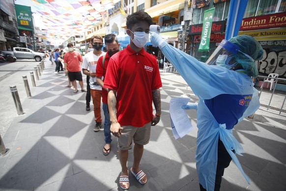 A health worker checks the temperature of a man falling in line for a COVID-19 swab test in Khaosan Road in Bangkok, Thailand Wednesday, April 14, 2021. Thailand recorded more than 1,000 COVID-19 infe ...