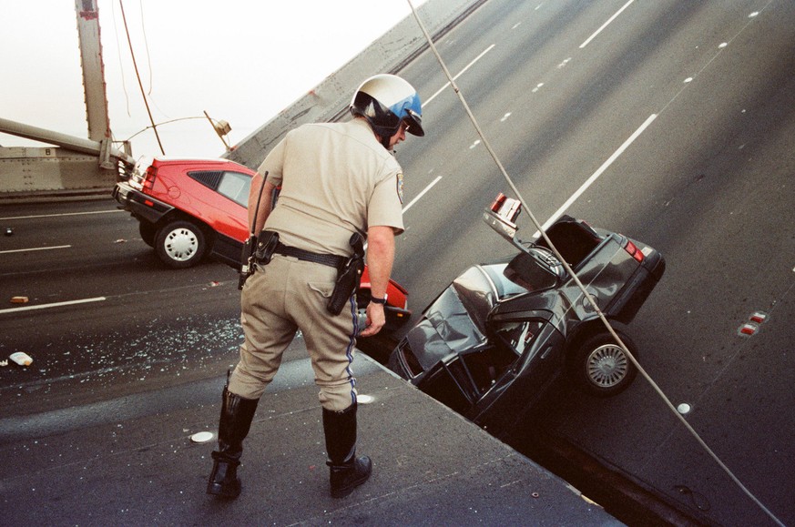 FILE - In this Oct. 17, 1989 file photo, a California Highway Patrol officer checks the damage to cars that fell when the upper deck of the Bay Bridge collapsed onto the lower deck after the Loma Prie ...