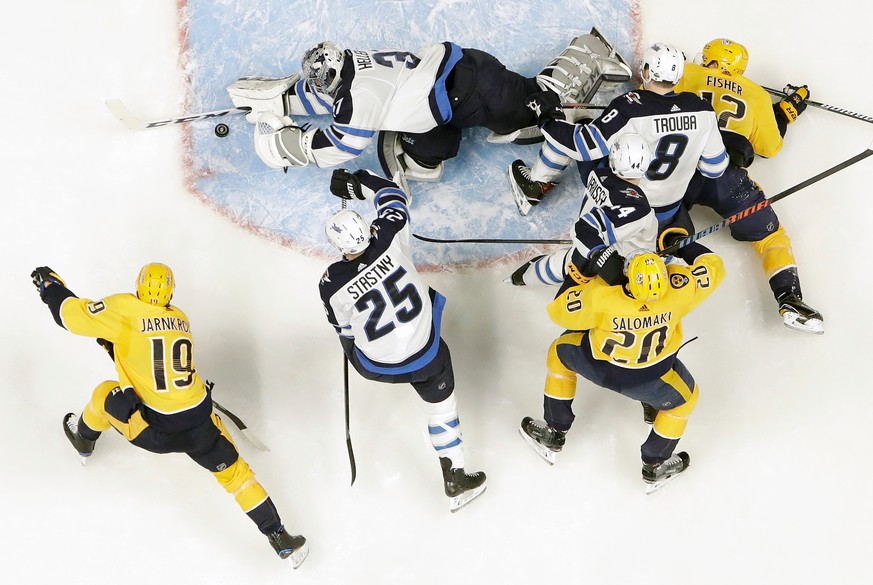 Winnipeg Jets goalie Connor Hellebuyck, top, blocks a shot as Nashville Predators center Calle Jarnkrok (19), of Sweden, watches for the rebound during the first period in Game 1 of an NHL hockey seco ...