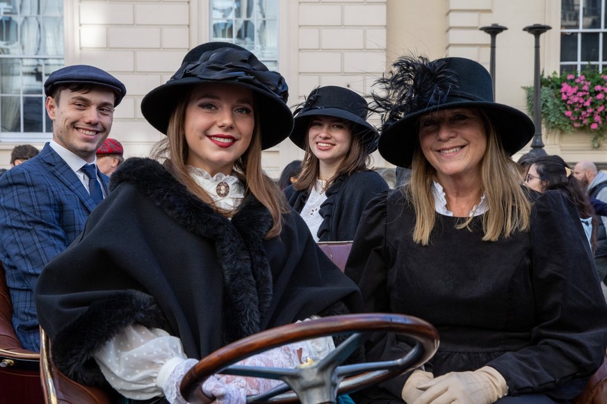 November 1, 2025, London, United Kingdom: Thee Ladies and one gentleman wearing traditional driving dress pose whilst sitting in a vintage car during a show. Thousands of people gathered on Pall Mall  ...