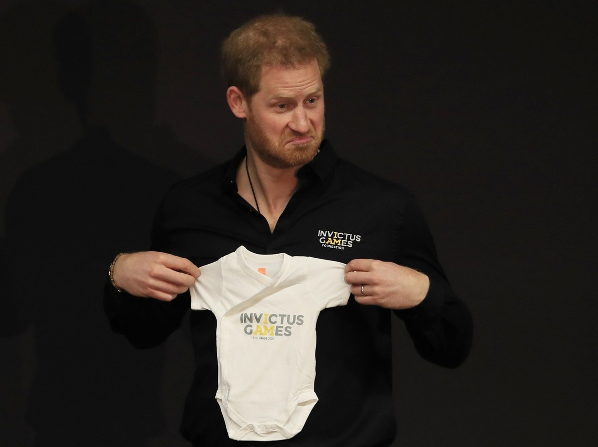 Britain's Prince Harry holds up an outfit for his newborn son, presented by Princess Margriet of the Netherlands, at the launch of the 2020 Invictus Games, in The Hague, Netherlands, Thursday, Ma ...