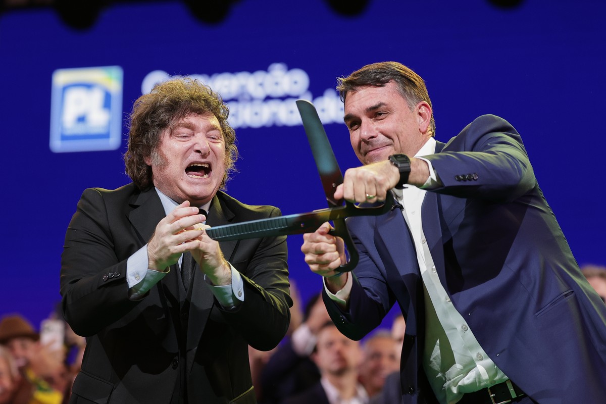 Brazilian Sen. Flavio Bolsonaro, right, handles an oversized pair of scissors, accompanied by Argentina's President Javier Milei during the Liberal Party convention where Bolsonaro was confirmed  ...