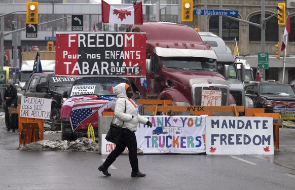 A woman crosses the street in front of vehicles parked as part of the trucker protest, Tuesday, Feb. 8, 2022 in Ottawa. Canadian lawmakers expressed increasing worry about protests over vaccine mandat ...