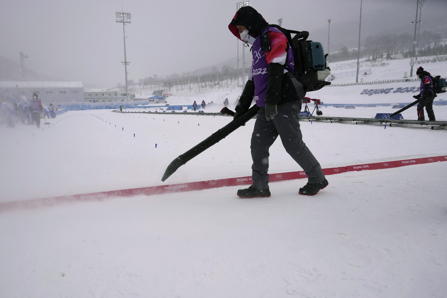 Workers clear the finish line of loose snow before the men&#039;s 4 x 10km relay cross-country skiing competition at the 2022 Winter Olympics, Sunday, Feb. 13, 2022, in Zhangjiakou, China. (AP Photo/A ...