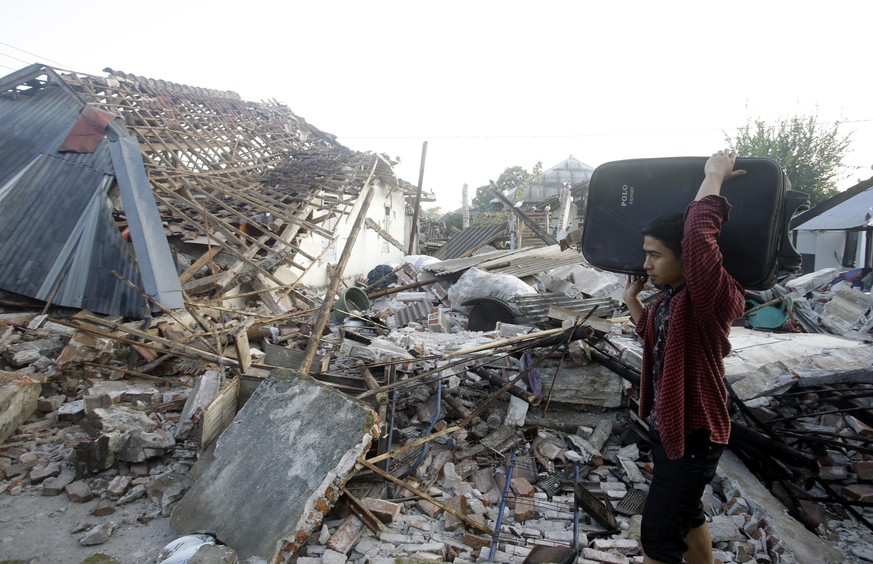 A man carries his belongings past the ruin of houses at a village affected by an earthquake in North Lombok, Indonesia, Thursday, Aug. 9, 2018. The north of Lombok was devastated by the powerful quake ...