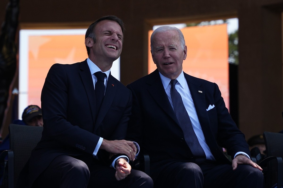 epa11393147 President Joe Biden and French President Emmanuel Macron laugh during a commemorative ceremony to mark D-Day 80th anniversary, Thursday, June 6, 2024 at the US cemetery in Colleville-sur-M ...
