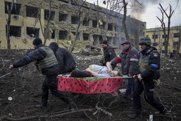 Männer tragen eine Frau aus einem zerstörten Spital in Mariupol, wo sie ihr Kind hätte gebären sollen. Sowohl das Baby als auch die Mutter überlebten den Angriff der Russen nicht.