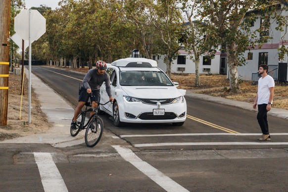 This Sunday, Oct. 29, 2017, photo provided by Waymo shows a Chrysler Pacifica minivan equipped with Waymo&#039;s self-driving car technology, being tested with the company&#039;s employees as a biker  ...