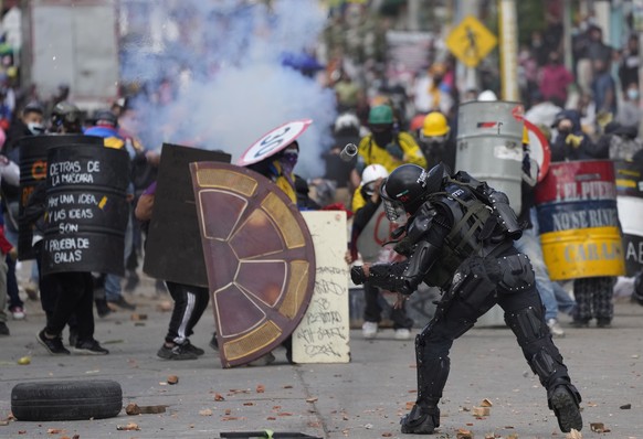 A police officer throws a stun grenade at protesters during an anti-government protest triggered by proposed tax increases on public services, fuel, wages and pensions in Bogota, Colombia, Monday, Jun ...