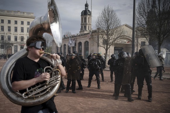 A protester plays music in front of police officers during a demonstration in Lyon, central France, Thursday, March 23, 2023. French unions are holding their first mass demonstrations Thursday since P ...