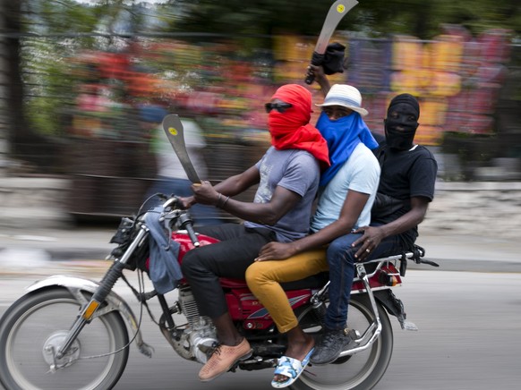 FILE - In this Feb. 24, 2020 file photo, men on a motorcycle brandish machetes as off-duty police officers protest over pay and working conditions, in Port-au-Prince, Haiti. A surge in violence is rat ...