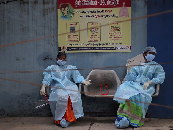 Medizinische Mitarbeiterinnen in Schutzausrüstung ruhen sich vor der Entnahme von Speichelproben für Covid-19-Tests aus. Foto: Mahesh Kumar A/AP/dpa