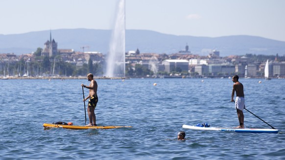 People paddle on their stand up paddle on Geneva Lake with the famous water fountain &quot;Le Jet d&#039;Eau&quot; and Cathedrale Saint Pierre are seen in background, in Cologny near Geneva, Switzerla ...