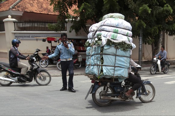 A Cambodian man, right, drive his motorbike overloaded with vegetable sacks as he passes a traffic police officer, center, in Phnom Penh, Cambodia, Tuesday, Aug. 25, 2015. (AP Photo/Heng Sinith)