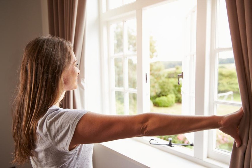 Eine Frau öffnet das Fenster: Schimmel droht. Der Flaschen-Test verrät, wann man lüften darf.