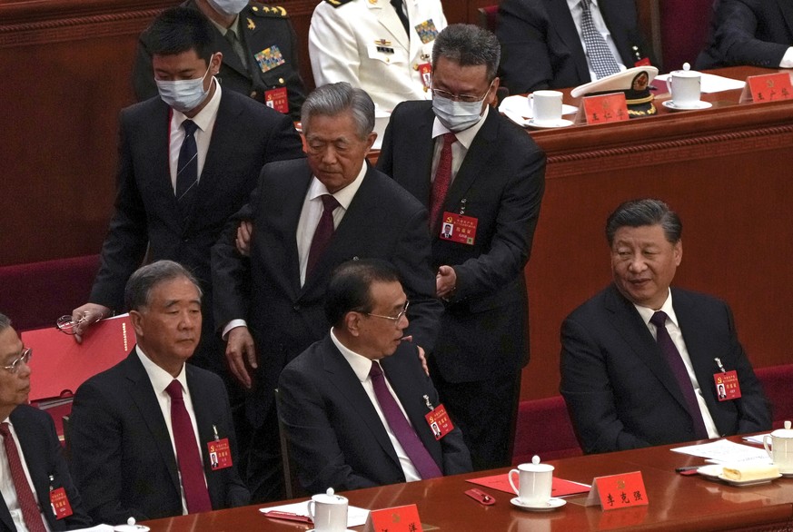 Former head of state Hu Jintao is led from the square by room stewards.  He sat next to party leader Xi Jinping (right).