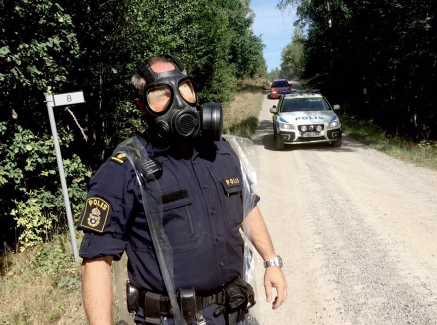 epa06962060 A police officer in a protective mask near the place where a Swedish Air Force Jas Gripen fighter jet crashed outside Ronneby, Sweden, 21 August 2018. According to reports, the airplane cr ...
