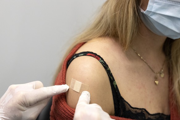 Ein Mitarbeiter des Impfzentrums klebt nach der Impfung ein Pflaster auf den Arm einer Frau, im Walk-In Impfzentrum auf dem BEA-Expo-Gelaende, am Dienstag, 21. Dezember 2021, in Bern. (KEYSTONE/Peter Klaunzer)
