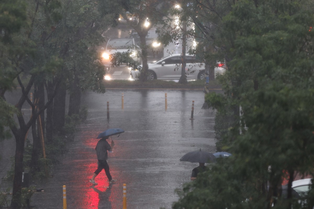 epa12399168 A person shelters under an umbrella from the rain while crossing the street during the afternoon in the wake of Typhoon Ragasa in Taipei, Taiwan, 23 September 2025. At least six individual ...