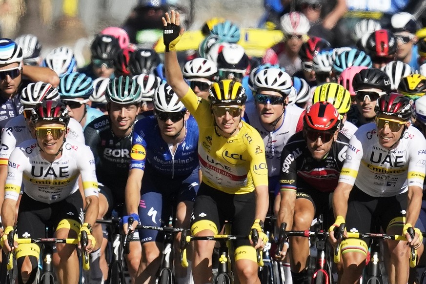 Slovenia&#039;s Tadej Pogacar, wearing the overall leader&#039;s yellow jersey, waves as he rides with his UAE Team Emirates teammates as they lead the pack during the twenty-first and last stage of t ...