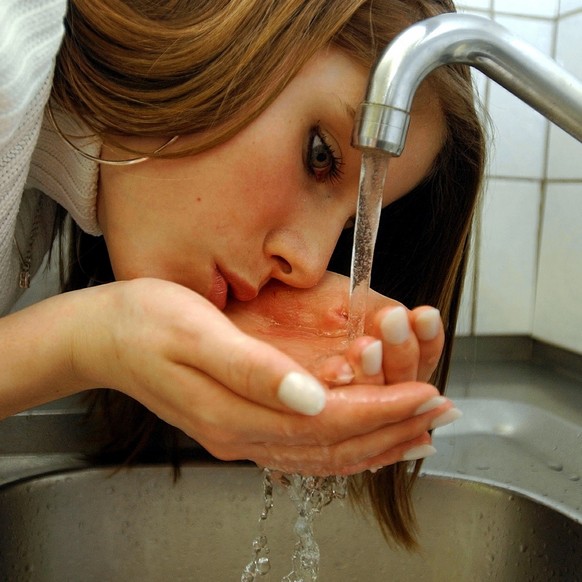 Eine junge Frau genehmigt sich einen Schluck Wasser aus dem Wasserhahn, aufgenommen in einer Kueche in Zuerich am 22. Maerz 2004. Schweizer Trinkwasser ist laut dem Zuercher Kantonslabor jedem Mineral ...