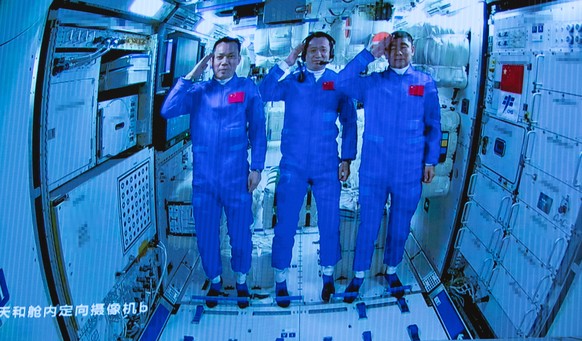 epa09281811 A screen image made available by Xinhua News Agency captured at the Beijing Aerospace Control Center shows three Chinese astronauts onboard the Shenzhou-12 spaceship saluting after enterin ...