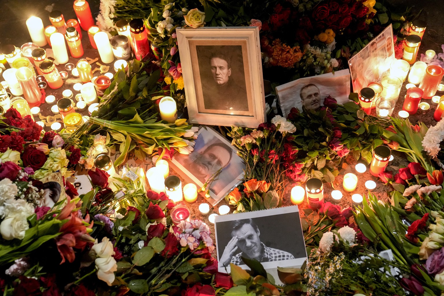 Photos of Russian opposition leader Alexei Navalny placed between candles and flowers on the ground in front of the Russian embassy during a protest in Berlin, Germany, Friday, Feb. 16, 2024. Russia&# ...
