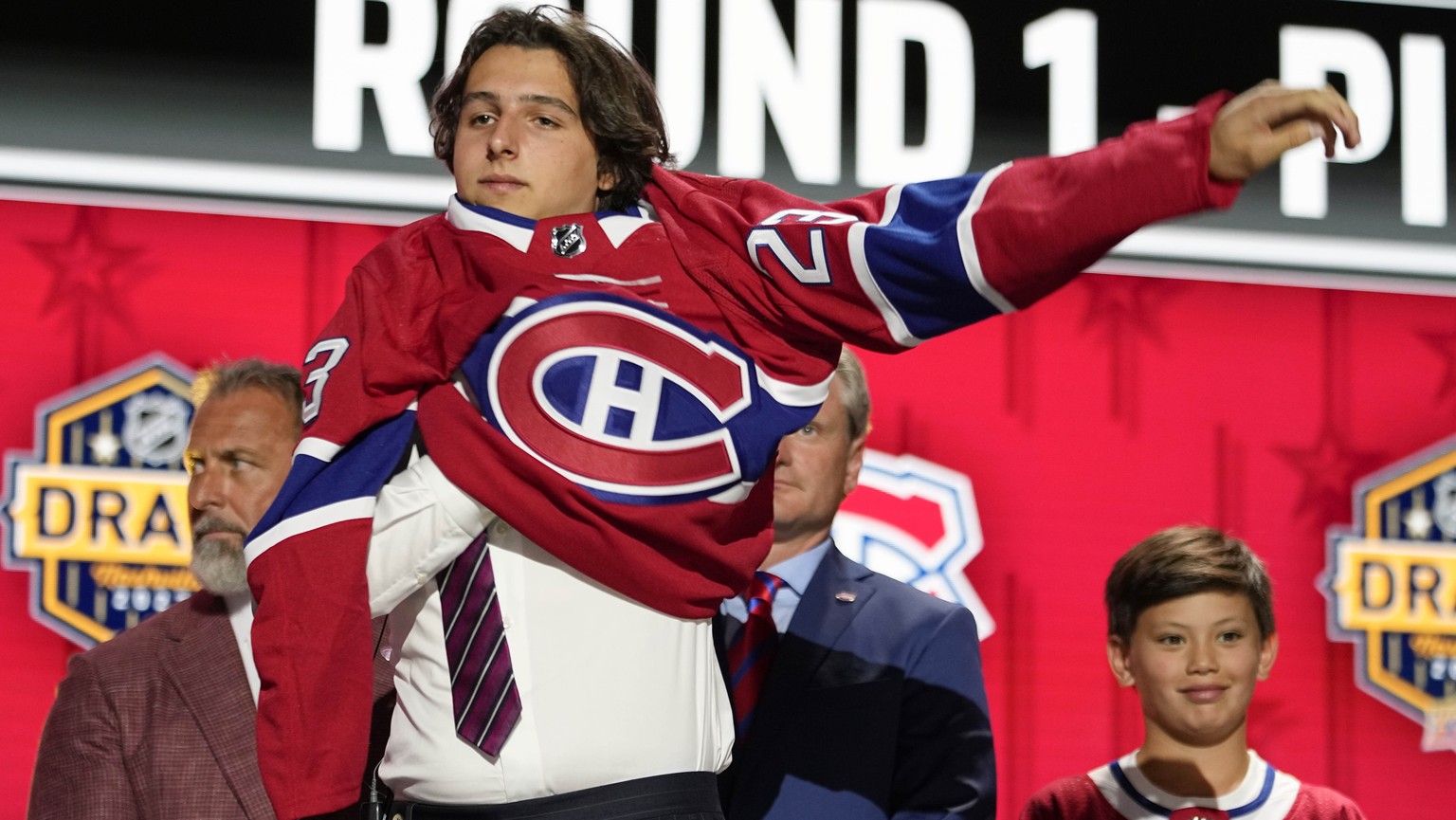 David Reinbacher puts on a Montreal Canadiens jersey after being picked by the team during the first round of the NHL hockey draft Wednesday, June 28, 2023, in Nashville, Tenn. (AP Photo/George Walker ...