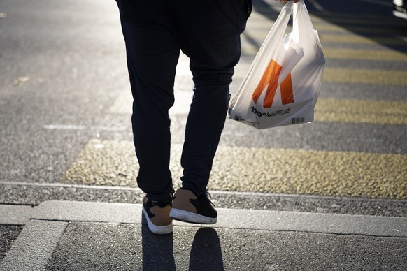 Ein Mann traegt eine Plastik- Einkaufstasche der Migros, die zu 100 % aus recyceltem Plastik besteht, fotografiert am Freitag, 29. November 2024 bei Zuerich. (KEYSTONE/Gaetan Bally)