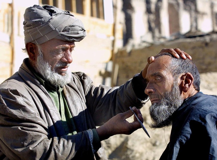 KABUL, AFGHANISTAN : An Afghan barber trims the beard of an Afghan man in the streets of the capital Kabul, 31 December 2001. With the fall of the Taliban there was a rush with men getting their beard ...