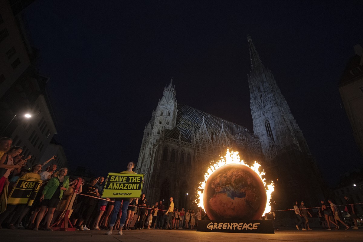 epa07795838 A Greenpeace activist displays a banner reading 'Save the Amazon' next to a burning earth installation in front of the St. Stephen's Cathedral (Stefansdom) during a protest  ...