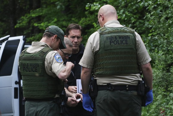 Washington State Fish and Wildlife Police confer with an individual from the King County Medical Examiner&#039;s and a King County Sheriff&#039;s deputy on a remote gravel road above Snoqualmie, WA.,  ...