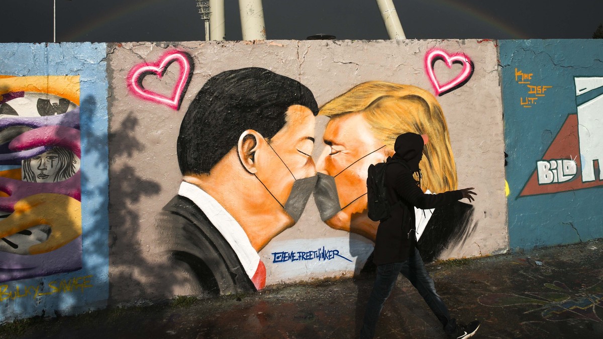 A man walks in front of graffiti depicting US President Trump, right, and China's President Xi Jinping kissing each other with face masks, displayed at a wall in the public park Mauerpark in Berl ...