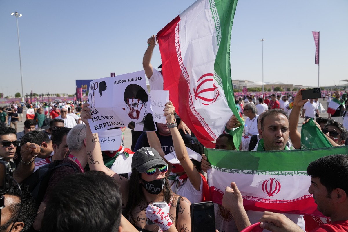Supporters wave Iranian flags and a woman holds up a sign reading "Freedom for Iran, No to Islamic Republic", ahead of the World Cup group B soccer match between Wales and Iran, at the Ahmad ...