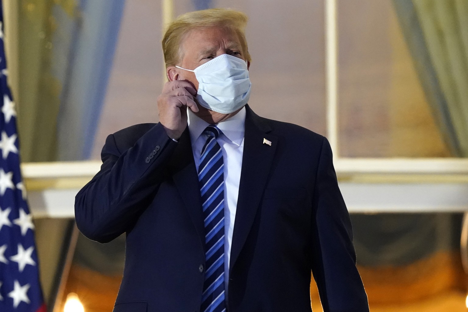 President Donald Trump removes his mask as he stands on the balcony outside of the Blue Room as returns to the White House Monday, Oct. 5, 2020, in Washington, after leaving Walter Reed National Milit ...