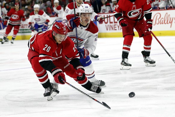 Carolina Hurricanes&#039; Sebastian Aho (20) tips the puck away from a charging Montreal Canadiens&#039; Cole Caufield (22) during the first period of an NHL hockey game in Raleigh, N.C., Thursday, De ...