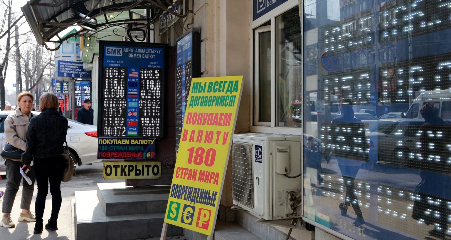 epa09824238 Kyrgyz people walk in front of a digital panel displaying the exchange rate for the euro and the US dollar at an exchange office in central Bishkek, Kyrgyzstan, 14 March 2022. Due to the g ...