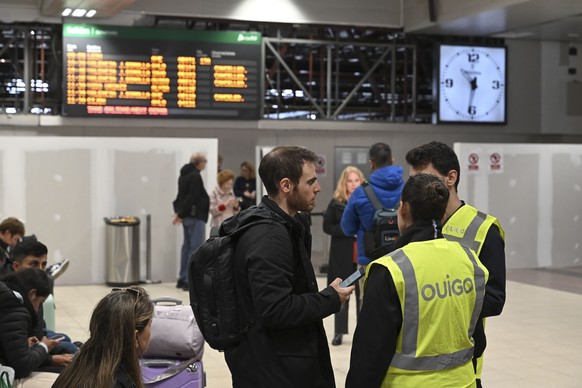 epa11692104 A traveler speaks with two employees of the Ouigo low-cost train service in front of information screens displaying the cancellation of train services between Madrid and Valencia at Chamar ...
