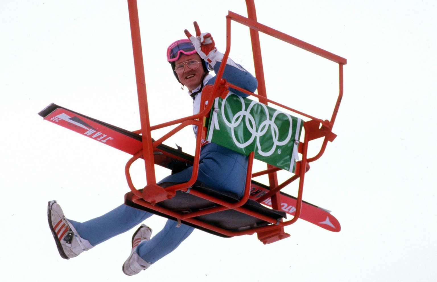 IMAGO / Sven Simon

Michael Edwards (Großbritannien) alias Eddie the Eagle grüßt mit dem Peace-Zeichen aus einem Sessellift / Der erste Brite, bei einem olympischen Skispringen war mehr Publikumsliebl ...