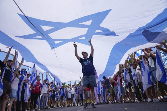 Demonstrators wave large Israeli flag during a protest against plans by Prime Minister Benjamin Netanyahu&#039;s government to overhaul the judicial system, outside the Knesset, Israel&#039;s parliame ...