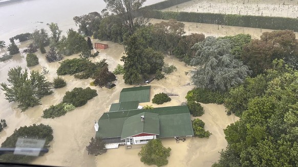 In this image released by the New Zealand Defense Force on Wednesday, Feb. 15, 2023, people stand on a rooftop of a home waiting to be winched to safety by helicopter in the Esk Valley, near Napier, N ...