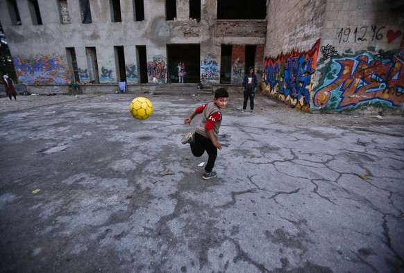 In this Saturday, May 12, 2018, picture, a migrant boy plays with a ball outside the abandoned building of a former student campus, destroyed during the Bosnian war, in the western Bosnian town of Bih ...