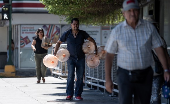 epa10716126 A man walks with jugs of water to be filled due to the high temperatures, in Monterrey, Nuevo Leon state, Mexico, 28 June 2023. The heat wave that hit Mexico has caused 36 deaths in the no ...