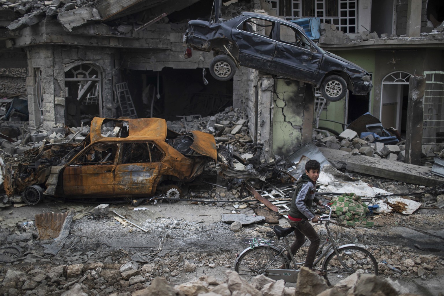 FILE - In this Sunday, March 19, 2017 file photo, a boy rides his bike past destroyed cars and houses in a neighborhood recently liberated by Iraqi security forces, on the western side of Mosul, Iraq. ...