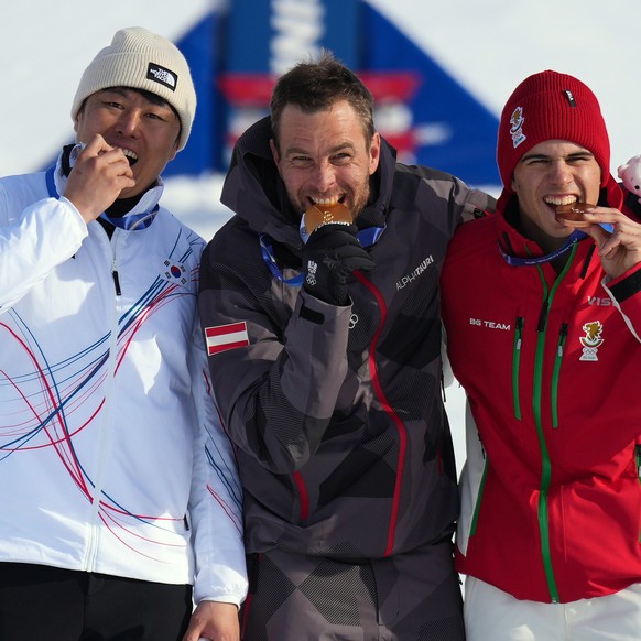 From left, silver medalist South Korea's Kim Sang-kyum, gold medalist Austria's Benjamin Karl and bronze medalist Bulgaria's Tervel Zamfirov bite their medals after the men's snowb ...