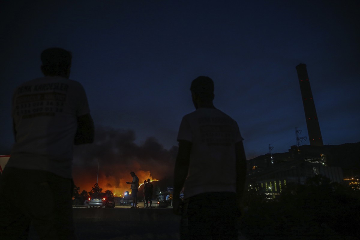 People stand in front of Kemerkoy Thermal Power Plant with the blaze approaching in the background, in Milas, Mugla, Turkey, Tuesday, Aug. 3, 2021. Turkish President Recep Tayyip Erdogan���s governmen ...