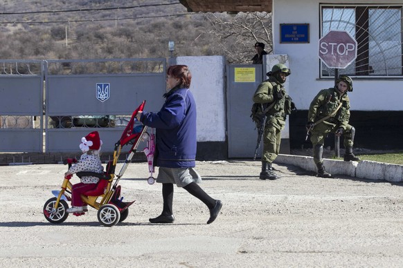 Eine Ukrainerin spaziert am 3. März im Dorf Perevalnoye bei Simferopol an mutmasslich russischen Soldaten vorbei.